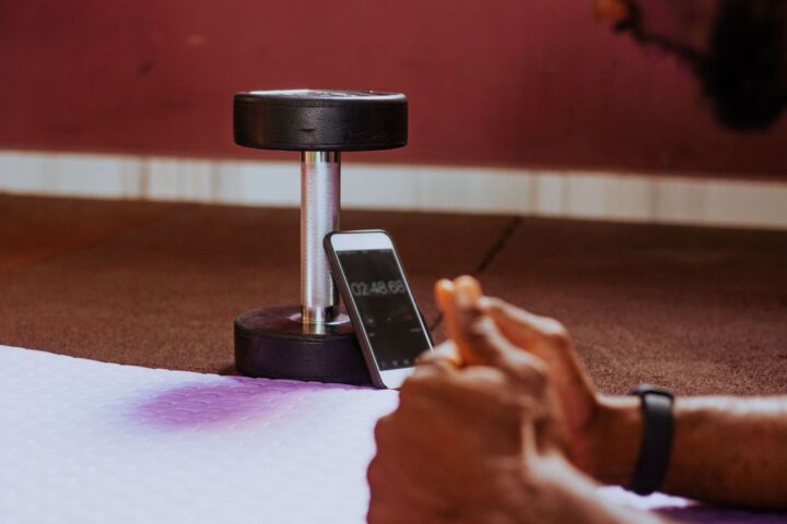 Man holding plank position looks at timer on smartphone, propped up on dumbbell