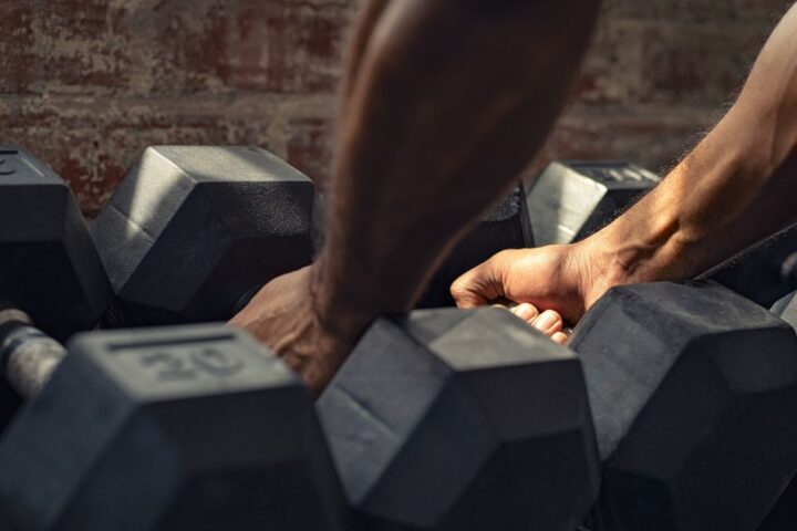 Hands picking up heavy dumbbells from rack