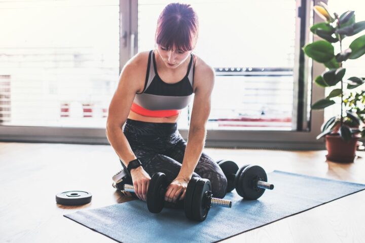 Kneeling woman adds weight plate to adjustable dumbbell