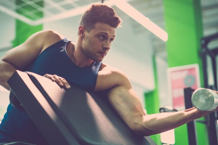 Man performing single-arm dumbbell preacher curl in gym