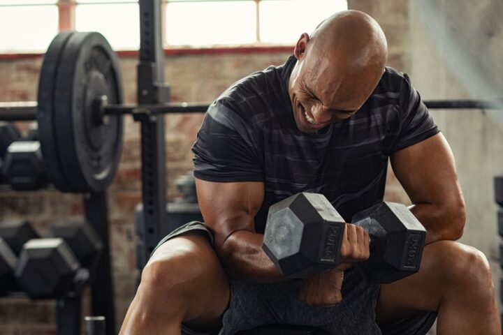Man grimacing with effort as he performs a concentration curl in a gym